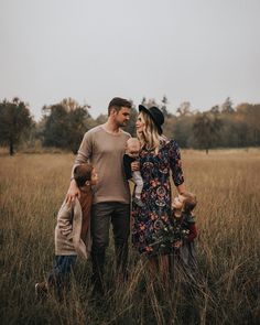 a man, woman and two children are standing in the middle of a field with tall grass