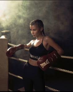 a woman wearing boxing gloves standing in front of a punching ring with her hands on the ropes