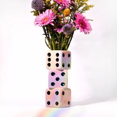 a vase filled with lots of pink flowers next to two dices on top of each other