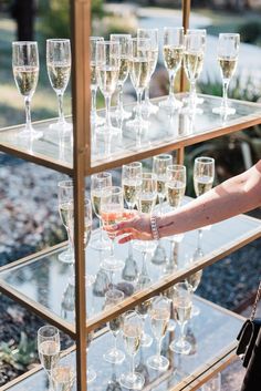 a display case filled with lots of wine glasses on top of a wooden table next to a woman's hand