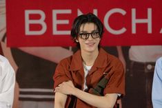 a young man with glasses standing in front of a sign and smiling at the camera