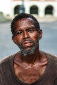 a man with tattoos on his chest stares at the camera while standing in front of a building