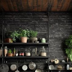 pots and pans are on the shelves in this industrial - style kitchen, with black brick walls