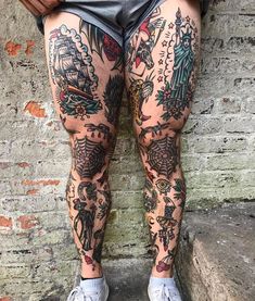 a person with tattoos on their legs standing next to a brick wall