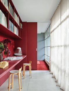 a room with bookshelves and two stools in front of a red wall