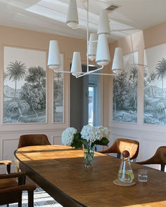 a dining room table with vases and flowers on it in front of large windows