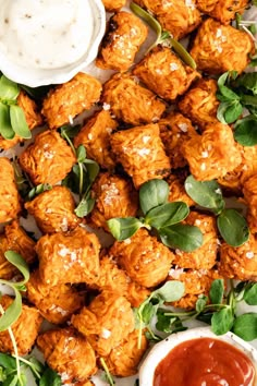 chicken bites with sauce and greens on a white platter next to dipping sauces