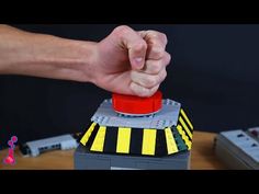 a hand holding a red button on top of a toy car with yellow and black stripes