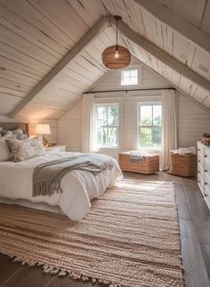 an attic bedroom with white walls and wood flooring is furnished with natural materials such as rugs, bedding, and pillows