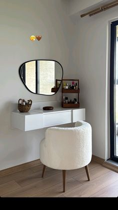 a white vanity with a round mirror on the wall and a stool in front of it