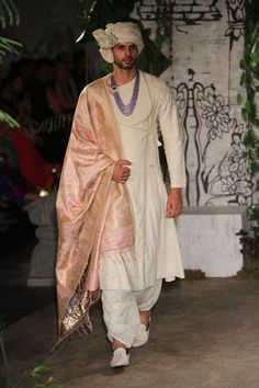 a man walking down the runway wearing a white outfit with gold and pink details on it