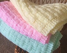 three blankets are stacked on top of each other in different colors and patterns, one is pink, the other is blue