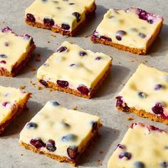 nine pieces of cake with white frosting and blueberries on top sitting on a baking sheet