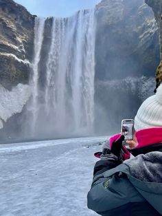 a person taking a photo with their cell phone in front of a waterfall and frozen water