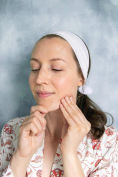 a woman with her eyes closed wearing a white headband and holding her hands to her face