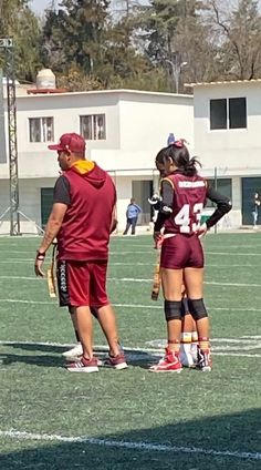 two girls in maroon uniforms are standing on the field with their hands behind their backs