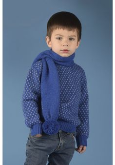 a young boy wearing a blue sweater and scarf, standing in front of a blue background