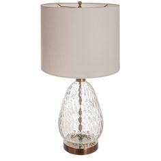 a clear glass table lamp with a white shade on the base and a gold metal base