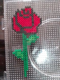 a red rose made out of legos on a clear plastic sheet with green stems