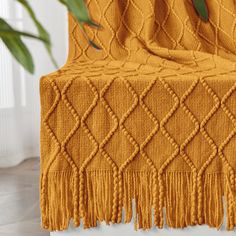 an orange knitted blanket with tassels on the back and sides, next to a potted plant