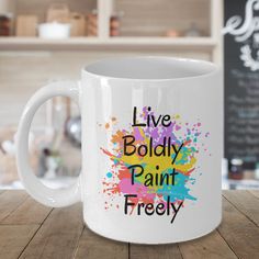 a white coffee mug with the words live boldly paint freely on it sitting on a wooden table