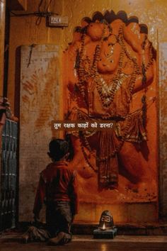 a man sitting on the ground in front of a wall with an image of hindu god