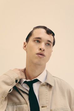 a man in a jacket and tie poses for the camera with his hands on his neck