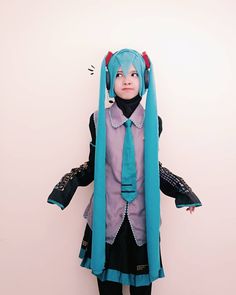 a person with blue hair wearing a dress and headpiece standing in front of a white wall