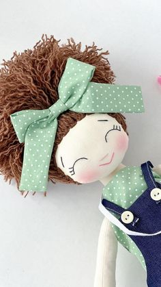 a doll with a green shirt and blue overalls next to a brown hair doll