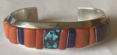 This is a fabulous signed Navajo Wes Willie sterling silver inlay multi-stone cuff bracelet. I am downsizing my personal collection and this cuff has never been worn. The absolutely stunning cuff features inlay of both red and orange Mediterranean coral, high-grade blue and green turquoise, sugilite, and lapis interspersed with sterling silver bars. The back is marked "Sterling" and "W" for the well-known Navajo master silversmith and inlayer Wes Willie. The inside of the cuff measures 5 1/2 inches from end-to-end with an opening of 1 1/4 inches which is NOT adjustable. The bracelet measures 3/4 inch at the widest point. It weighs 2.28 ounces or 64.5 grams. Add this beautiful and collectible cuff bracelet to your collection! Free USPS Registered Insured Mail shipping to the United States. Southwestern Inlay Cuff Bracelet Gift, Artisan Rectangular Bracelets As Gifts, Handmade Rectangular Cuff Bracelet For Gifts, Handmade Rectangular Cuff Bracelet As Gift, Handmade Rectangular Cuff Bracelet Gift, Handmade Southwestern Cuff Bracelet As Gift, Free Sign, Red And Orange, Silver Bars