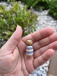 a tiny figurine in the palm of someone's hand with some plants behind it