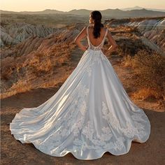 a woman in a white wedding dress standing on top of a dirt hill with her back to the camera