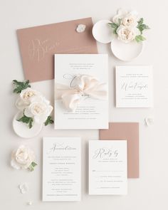 the wedding stationery is laid out on top of each other, with white flowers and greenery