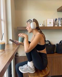 a woman sitting at a table with headphones on and holding a cup in her hand