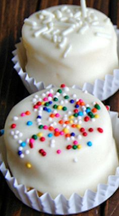 two cupcakes decorated with white frosting and sprinkles on a wooden table