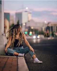 a woman is sitting on the curb with her hair blowing in the wind