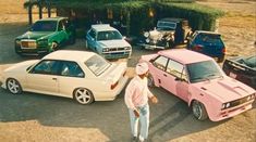 several cars parked in a parking lot with one person standing next to the pink car