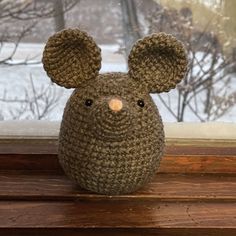 a crocheted mouse sitting on top of a window sill next to a snow covered tree