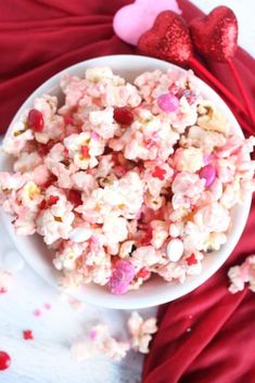 a white bowl filled with pink and red popcorn next to two hearts on a table