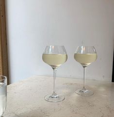 two wine glasses filled with white wine sitting on a table next to a glass of water