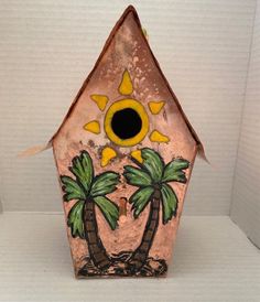 a pink birdhouse with palm trees painted on it's side and sun above the roof