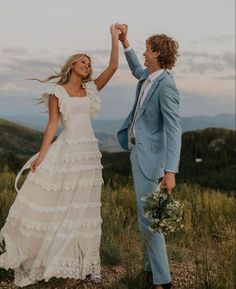 a man and woman holding hands while standing on top of a hill