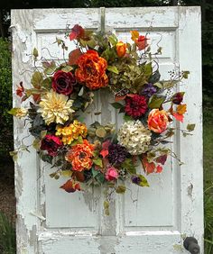 an old door with a wreath on it that has flowers and leaves all over it