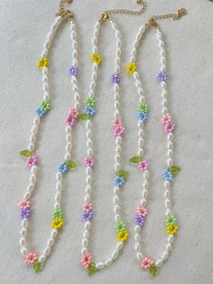 three necklaces with flowers and leaves are on a white tablecloth next to a pair of scissors