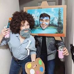 two people dressed up in costumes and holding paintbrushes, one with a painting on it's face