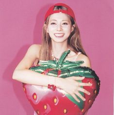 a woman in a red hat and dress holding a large strawberry shaped balloon with her arms wrapped around it