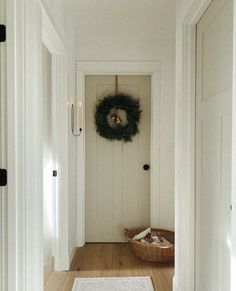 a white door with a wreath on it and a basket in the hallway next to it