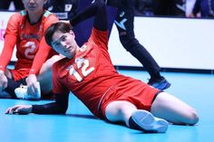 two men in red uniforms playing volleyball on a court with people watching from the sidelines