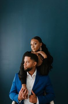 a man sitting on the back of a woman's shoulders in front of a blue wall