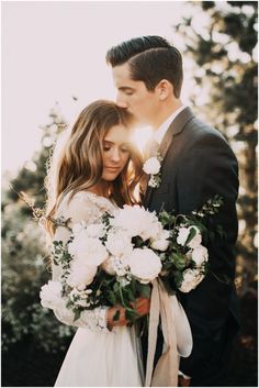 a man and woman standing next to each other in front of trees with white flowers